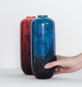 Cylindrical vase with a mottled deep blue finish, shown next to a red version