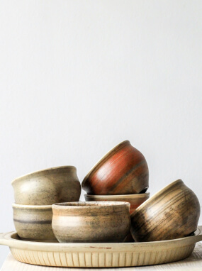 Small rustic bowls in brown, rust and sand glazes stacked on a shallow round tray